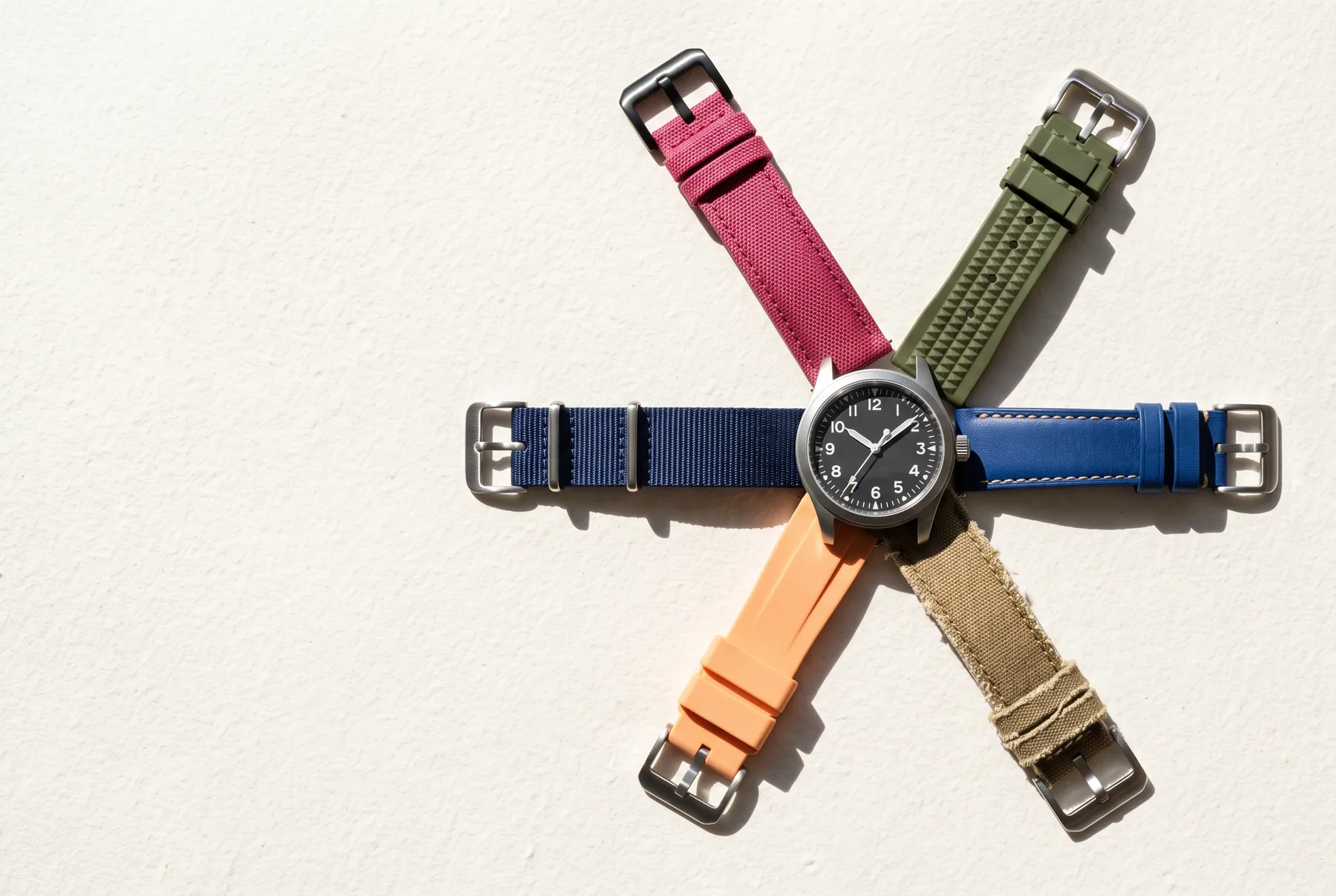 A field watch surrounded by six straps in different colours